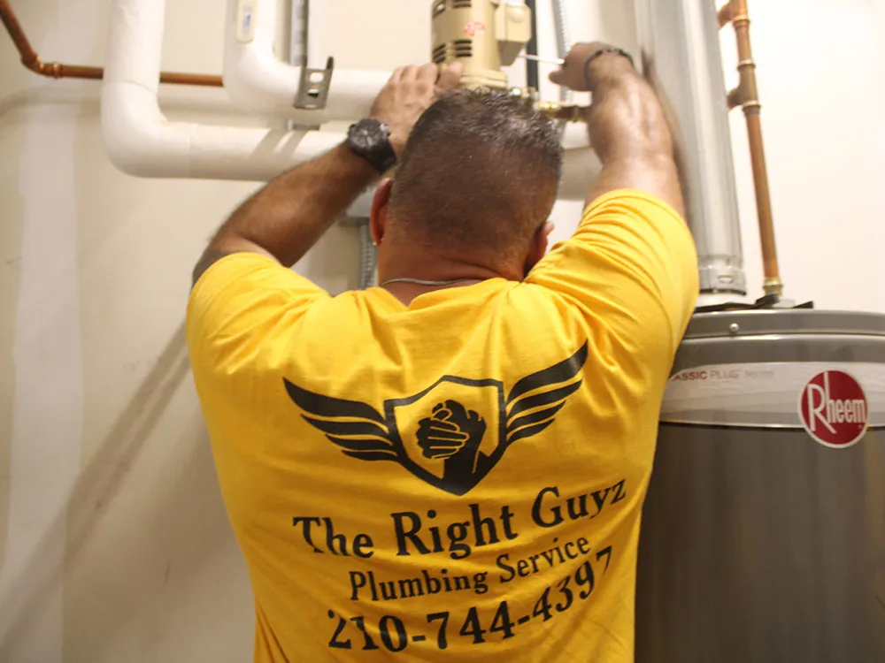 Un plomero de The Right Guyz con camisa de la compañía revisando las líneas de agua arriba de un calentador