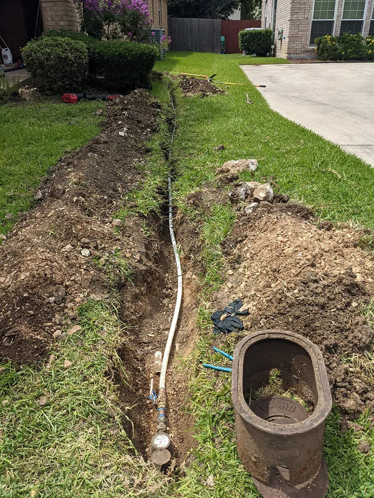 A new water service line laid in a trench along a front yard sidewalk