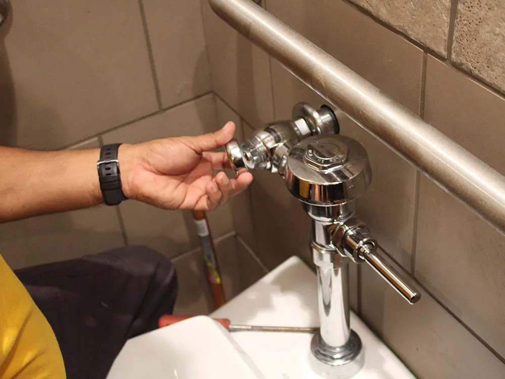 A plumber servicing a commercial flush valve