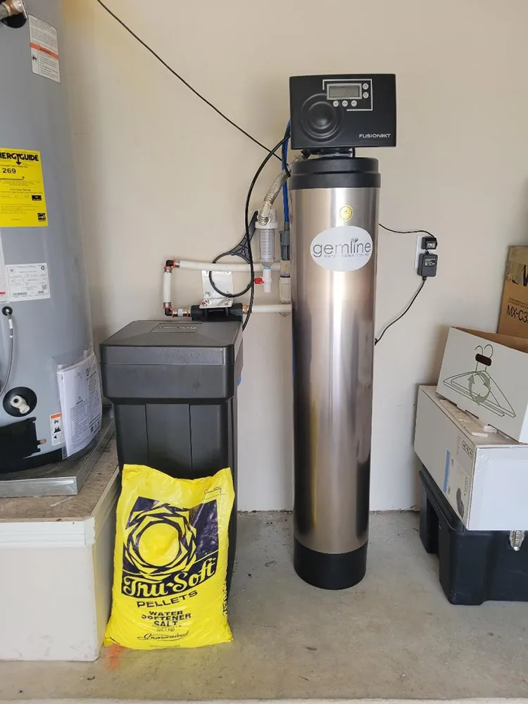 A new water softener and brine tank installed beside a water heater in a garage