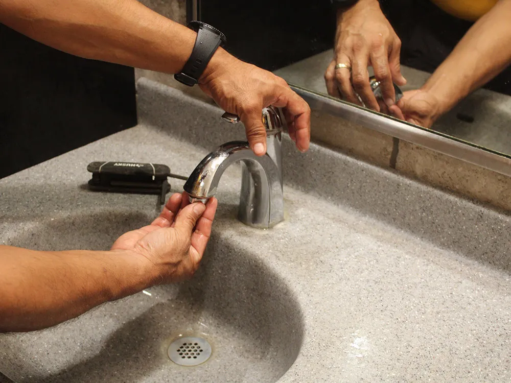 Un plomero instalando una llave nueva en el lavabo de un baño comercial